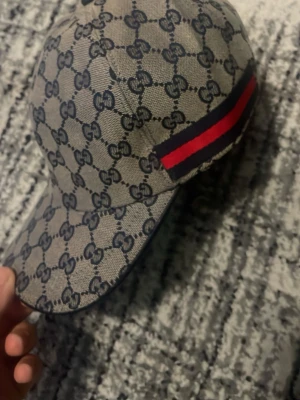 Gucci keps med monogram och röd-blå rand - Snygg keps från Gucci med klassiskt GG-monogram i beige och mörkblått. Kepsen har en röd och marinblå rand på sidan och är tillverkad i canvasmaterial. Perfekt accessoar för en trendig streetstyle-look.  Medföljer GG låda dust bag och alla papper princip splitterny skick 
