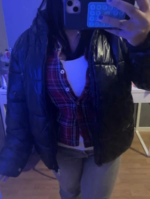 Svart pufferjacka från 157, M - Säljer en svart pufferjacka från 157 i storlek M. Jackan har en klassisk pufferdesign med glansigt yttertyg och breda kanaler. Perfekt för kalla dagar och enkel att matcha med olika outfits. Jackan har dragkedja framtill och hög krage.