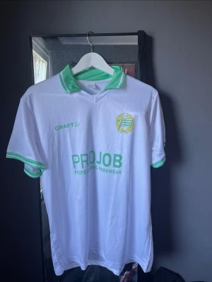 Hammarby matchtröja - Säljer en vit Hammarby matchtröja från Craft med gröna detaljer på krage och ärmslut. Tröjan har klubbmärke på bröstet och sponsorlogga 'PROJOB' framtill. Perfekt för dig som vill stötta laget på match eller träning.