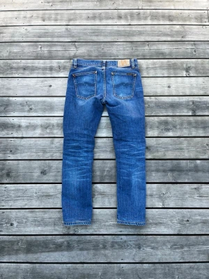 Blå jeans från Nudie Jeans - Säljer ett par klassiska blå jeans från Nudie Jeans med raka ben och femficksmodell. Perfekta för en avslappnad och trendig look. Strl: 28:30. Bra skick. Fråga vid funderingar!