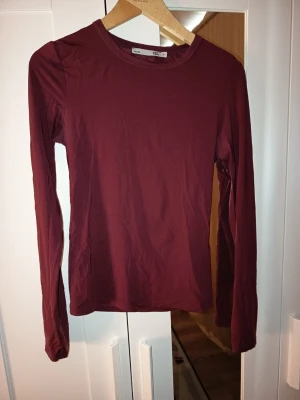 Mörkröd långärmad topp  - En enkel och stilren mörkröd långärmad topp från Lager 157. Toppen har rund halsringning och är figurnära i modellen. Perfekt att matcha med jeans eller kjol för en clean look.