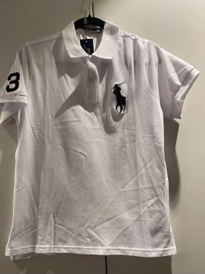 Polo Ralph Lauren vit piké med stor 3 på ärmen - Ny med taggar - Stl M" - Helt ny vit Polo Ralph Lauren piké i storlek M. Stor marinblå trea på vänster ärm + klassisk broderad marinblå Polo Player-logga på bröstet. Kommer med alla taggar kvar, aldrig använd. Bra kvalitet, tidlös stil. Hör av dig vid frågor😊👕