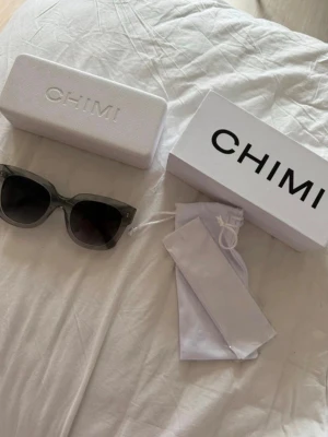 Svarta solglasögon från CHIMI - Stilrena solglasögon från CHIMI med fyrkantig båge och mörka glas. Kommer med originalfodral och förvaringspåse. Perfekta för att lyfta din look under soliga dagar.