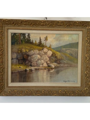 Oljemålning av Ejnar Kohlmann, 57x46cm - Vacker tavla / målning av kände finländske konstnären Einar Kohlmann (1888–1968) med naturmotiv. Olja på duk, i utsmyckad guldfärgad ram. Målningen föreställer ett fridfullt landskap med vatten, klippor och träd. Mått: 57 cm x 46 cm. Härlig tavla som förgyller vilket rum som helst. 