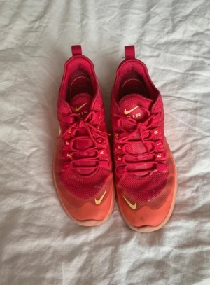 Nike Air Max röd-orange sneakers - Säljer ett par Nike Air Max sneakers i en snygg röd och orange färgkombination med gula detaljer. Skorna har en synlig Air-sula, mesh- och syntetmaterial samt klassisk snörning. Perfekta för dig som vill sticka ut med färg på fötterna.