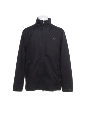 Svart vindjacka från Fred Perry - Svart vindjacka från Fred Perry med dragkedja framtill, hög krage och två fickor med dragkedja. Jackan har diskret logga på bröstet och justerbara ärmslut med tryckknappar. Perfekt för blåsiga dagar och enkel att matcha.