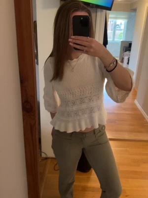 Vit virkad blus med volang - Söt vit blus med virkade detaljer och volang nedtill. Blusen har trekvartsärm och ett lätt genombrutet mönster som ger en romantisk känsla. Perfekt att matcha med både jeans och kjol för en trendig look.