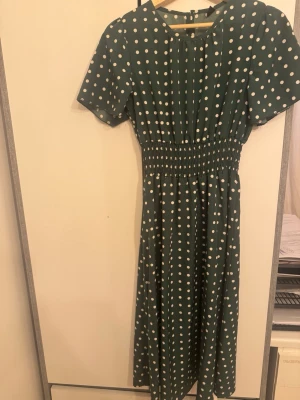 Grön prickig midiklänning från SHEIN - Grön midiklänning från SHEIN med vita prickar, korta ärmar och smock i midjan som ger en snygg siluett. Klänningen har rund halsringning och ett luftigt fall, perfekt för varma dagar. Klassisk och lekfull design som sticker ut.