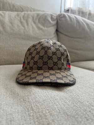 Navy blue GG Keps - Säljer en beige keps  med det klassiska GG-monogrammet över hela kepsen. På sidan finns en röd och marinblå rand som ger extra