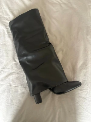 Svarta stövletter med klack - Snygga svarta stövletter i slätt konstläder med hög blockklack och spetsig tå. Dragkedja på insidan för enkel påtagning och en något lösare skaftdesign som ger en cool look.