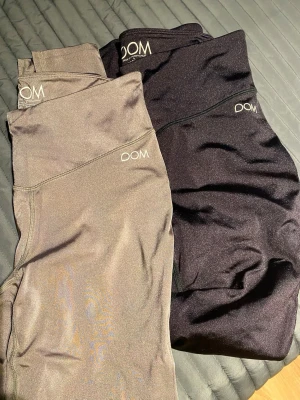 NYA shiny träningstights från Drop of Mindfulness - Två par träningstights från Drop of Mindfulness, ett par i svart och ett par i beige. Tillverkade i stretchigt material med 82% polyamid och 18% elastan. Perfekta för gymmet eller yoga, med hög midja och bekväm passform. Squat proof och full längd. Aldrig använda.