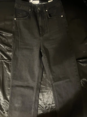 Svarta raka jeans med hög midja - Snygga svarta jeans med rak passform och hög midja. Klassisk femficksmodell med knapp och dragkedja framtill. Jeansen har en stilren look och passar perfekt till alla typer av outfits. Materialet är denim i bomull.