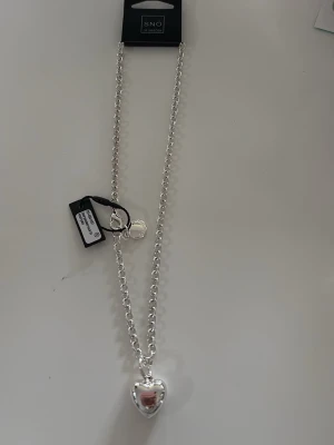 Silverhalsband med hjärthänge från SNÖ - Snyggt silverfärgat halsband från SNÖ of Sweden med ett blankt hjärthänge. Fixk den i konfirmation present men den kommer nt till användning den ör aldrig använt har fortfarande lådan men inget kvitto så jag kunde byta den. pris kan diskuteras!!