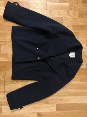 Marinblå kappa med guldknappar - Fin marinblå skepparkappa från Gina young med guldknappar framtill. Inte använts mycket. Pris kan diskuteras.