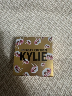 Kylie Holiday Edition puder - Exklusiv highlighter från Kylie Holiday Edition i en snygg guldförpackning med läppmotiv. Kommer i en rund, svart dosa med guldtext. Perfekt för att ge glow till din makeup och skapa en lyxig finish.