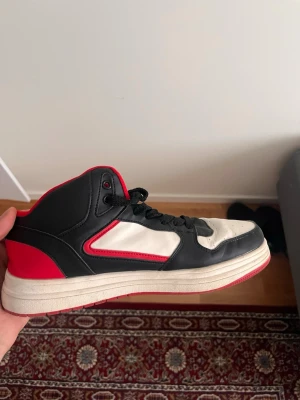sneakers - Snygga high top sneakers i svart, vitt och rött med klassisk siluett. Skon har svart ovandel i konstläder, vita paneler och röda detaljer samt röd yttersula. Svarta skosnören och vadderad krage för extra komfort.