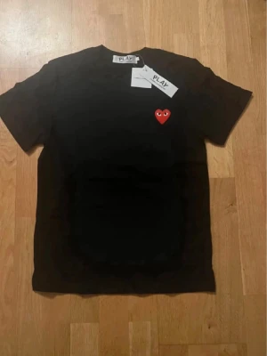 Svart Comme des Garçons PLAY t-shirt - Svart t-shirt från Comme des Garçons PLAY med det ikoniska röda hjärtat med ögon broderat på bröstet. Klassisk passform och rund halsringning. Tillverkad i mjuk bomull, perfekt för en clean och stilren look.