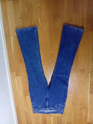 Blå utsvängda jeans - Säljer ett par klassiska blå jeans med utsvängda ben och hög midja. Jeansen har en enkel design utan synliga loggor och är tillverkade i denim. Perfekta för dig som gillar retrostil och vill ha ett par bekväma jeans med 70-talsvibbar.