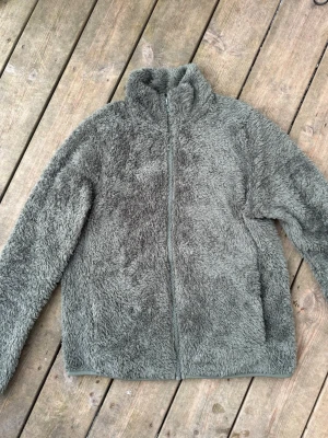 Grön uniqlo Fluffy fleece  teddyjacka med dragkedja - grön Fluffy fleece från uniqlo. Xs.   med hög krage och hel dragkedja framtill. Jackan har två sidofickor och är gjord i mjukt, teddyliknande material som håller dig varm och bekväm. Perfekt för dig som gillar en avslappnad och trendig stil.