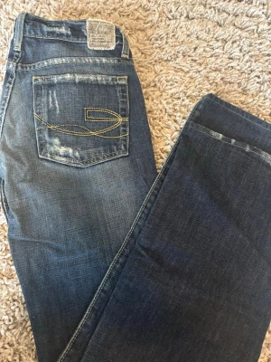 Mörkblåa bootcut jeans - Mörkblåa bootcut jeans från märket Cip pepper. Jeansen har fina sydda mönster på fickan med lite ”hål” i byxorna här och där. Skulle säga att dem är lite mer på det kortare hållet. Mått: Midjemått tvärs över knappen 38cm. Från grenen upp till linningen 20cm. Innebenslängden 77cm. Ytterbyxlängden 96cm. Hör av dig om du har några frågor eller funderingar❤️
