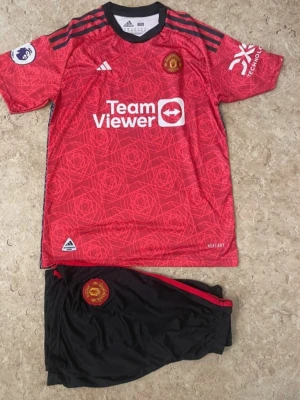Manchester United Rashford matchställ - Säljer ett Manchester United matchställ från Adidas med Rashford #10. Tröjan är röd med svarta detaljer, klubbmärke och sponsorloggor, samt ett mönster i rött. Shortsen är svarta med röd rand och klubbmärke. Materialet är lätt och andas, perfekt för fotbollsträning.