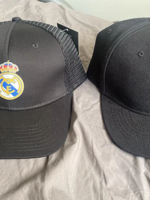 Svart Real Madrid keps och totenham - Snygg svart keps med Real Madrid-logga framtill. Kepsen har böjd skärm och mesh på sidorna för extra ventilation. Perfekt för dig som vill visa ditt stöd för laget och samtidigt hålla stilen. Justerbar passform baktill. Totenham keps, en för 80 och båda för 140. Helt nya