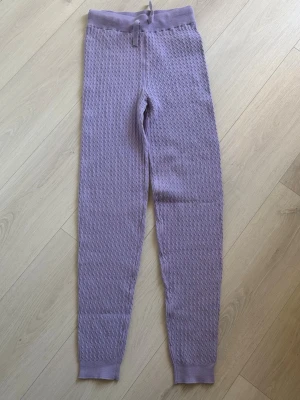 Lila stickade loungewearbyxor - Mysiga lila loungewearbyxor från Cubus med kabelstickat mönster. Byxorna har ribbad midja med dragsko och ribbade benslut. Perfekta för chill hemma och riktigt sköna tack vare det mjuka materialet. Storlek 170