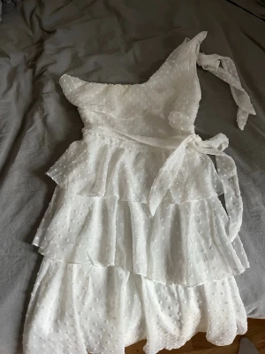 Vit oneshoulder klänning från SHEIN - Söt vit oneshoulder klänning från SHEIN med volangdetaljer och knyt i midjan. Klänningen har ett diskret prickigt mönster.