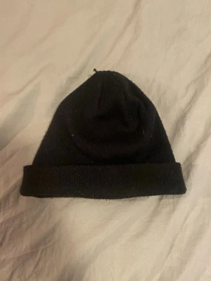 Svart ribbad mössa från Åhléns - En klassisk svart ribbstickad mössa från Åhléns. Mössan har uppvikt kant och är tillverkad i mjukt material som sitter skönt på huvudet. Enkel och stilren design som passar till det mesta.