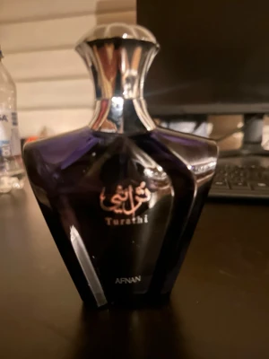 Afnan Turathi parfymflaska - Snygg parfymflaska från Afnan, modell Turathi. Flaskan är mörklila med silverfärgat lock och har en elegant, kantig form. Text i både arabiska och engelska på framsidan ger en lyxig känsla. Perfekt för dig som gillar exklusiva dofter. Cirka 70 ml kvar av 90ml.