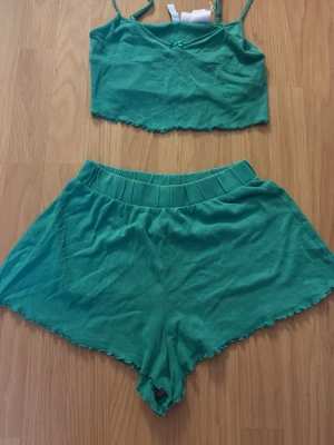 Grönt set från Divided med topp & shorts - Sött grönt underklädesset från H&M med en croppad topp med smala axelband och liten rosett framtill samt matchande shorts med bred resår i midjan. Båda delarna har vågig kant och är gjorda i mjukt bomullsmaterial. Perfekt för en chill och bekväm look.