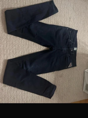 Mörkblå slim fit jeans från Replay - Snygga mörkblå slim fit jeans från Replay med klassisk femficksdesign och diskret logga på bakfickan. Jeansen har normal midja och raka ben, perfekta till en avslappnad stil. Tillverkade i mjukt denimtyg för skön känsla.