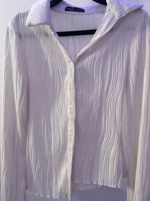 Vit ribbad skjorta - Vit skjorta med ribbad/veckad struktur som gör att den sitter fint på kroppen. Enkel men ändå lite annorlunda jämfört med en vanlig skjorta. Passar bra både till vardag och om man vill klä upp sig lite.