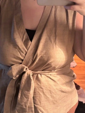 Beige set med omlottopp och byxa - Säljer ett snyggt beige set med omlottopp som knyts i midjan och matchande vida byxor med resår i midjan. Setet har en avslappnad passform och är gjort i ett mjukt, vävt material som känns luftigt. Perfekt för dig som gillar stilrena och bekväma plagg.