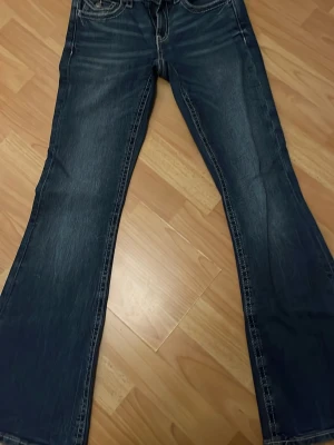 Mörkblå bootcut jeans med detaljer - Snygga mörkblå bootcut jeans med slitningar och kontrastsömmar. Baksidan har två fickor med dekorativa sömmar och knappar. Klassisk femficksmodell i denim, perfekta till en avslappnad stil. Dom är ifrån Gina Young storlek M fast passar för Xs o S