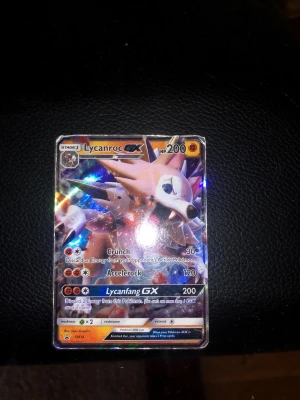 Pokémonkort Lycanroc GX holografisk - Säljer ett holografiskt Pokémonkort med Lycanroc GX. Kortet har färgstarka effekter och visar Lycanroc i en actionfylld pose. Det är ett samlarkort med attacker som Crunch, Accelerock och Lycanfang GX. Perfekt för samlare eller Pokémonfans.