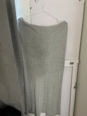 Grå långkjol med slits - En enkel och stilren grå långkjol i mjukt bomullsmaterial. Kjolen har en rak passform och en slits baktill för extra rörelsefrihet. Perfekt att matcha med en crop top eller hoodie för en chill look.