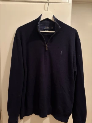 Mörkblå cashmere-tröja Polo Ralph Lauren - Snygg mörkblå stickad tröja från Polo Ralph Lauren i 100% cashmere. Tröjan har halv dragkedja, hög krage och diskret broderad logga på bröstet. Perfekt för dig som vill ha en klassisk och lyxig look.