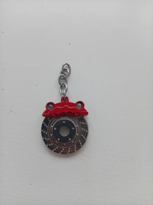 Bilbromsskiva nyckelring  - Nyckelring form av en bromsskiva med röd bromsok, tillverkat i metall. Perfekt för dig som gillar bilar och vill ha något