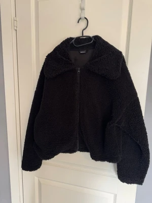 Svart teddyjacka - Mysig svart teddyjacka med dragkedja framtill och stor krage. Jackan har en oversized passform och är gjord i fluffigt teddy-material..