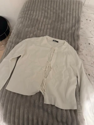 Vit tröja med knytning framtill - Trendig vit cardigan med långa ärmar och öppen front som knyts med flera band. Enkel och stilren design som passar perfekt till många outfits. Mjuk och bekväm, perfekt för lager-på-lager-stil. Storlek xs använd 1 gång.