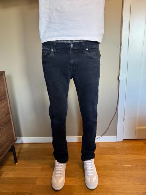 Svarta slim fit jeans från Nudie  - Säljer ett par svarta slim fit jeans från Nudie. Jeansen har klassisk femficksmodell, normal midja och raka ben. Tillverkade i mjuk denim med stretch för extra komfort. Perfekta till sneakers och t-shirt för en clean look.