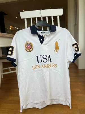 Vit pikétröja från Ralph Lauren - Vit pikétröja från Ralph Lauren med mörkblå krage och detaljer. Vintage stuk. Storlek XL men passar om man är L eller gillar overzied