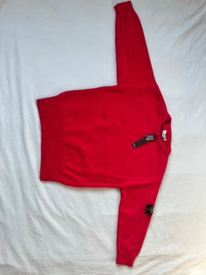Röd stickad tröja från Gant - Riktigt snygg röd stickad tröja från Gant med klassisk rund halsringning och ribbade muddar vid ärmslut och nederkant. Perfekt för dig som gillar stilrena och färgstarka plagg. Tröjan har en enkel design och är tillverkad i mjukt material.