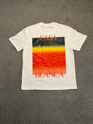 Vit t-shirt från Casablanca - Vit t-shirt från Casablanca med färgstarkt tryck i svart, gul och röd på både bröstet och ryggen. Klassisk passform och rund halsringning. Perfekt för dig som vill sticka ut med en snygg och modern look.