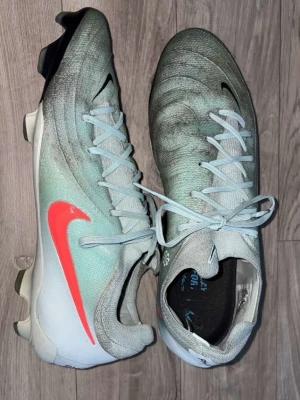 Nike Mercurial fotbollsskor ljusgrå - Snygga Nike Mercurial fotbollsskor i ljusgrått med svart och vit detalj samt en stor röd Nike-swoosh på sidan. Skorna har snörning och är tillverkade i syntetmaterial för bra passform och grepp på planen. Perfekta för dig som vill sticka ut på fotbollsplanen. Har använt den lite men den har inga skador. Priset är inte i hugget så, kan diskuteras 