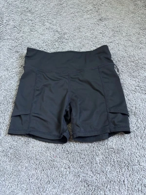 Träningsshorts soc - Säljer ett par svarta träningstights shorts med hög midja och fickor på sidorna. Perfekta för gymmet eller löprundan. Stretchigt material som sitter skönt och följer kroppen.
