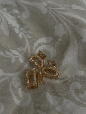 Guldig hårklämma med glitterdetaljer - Snygg hårklämma i guld med rektangulär och oval form, täckt av glittrande stenar som ger en lyxig känsla. 