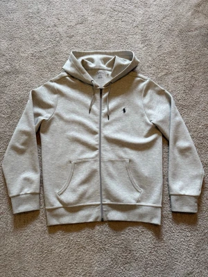 Hoodie Ralph Lauren - Säljer denna gråa Zip-Hoodie från Ralph Lauren i storlek M. Knappt använd då den är för stor för mig, så skicket är som nytt. Nypris 2000kr. 