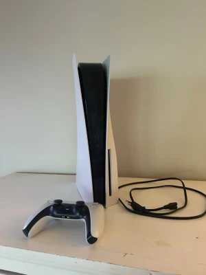 PlayStation 5 med handkontroll - PlayStation 5 konsol från Sony i vit och svart design med stilrena, böjda paneler. Medföljer en trådlös DualSense-handkontroll och strömkabel. Perfekt för gaming på nästa nivå med grym prestanda och snygg look.